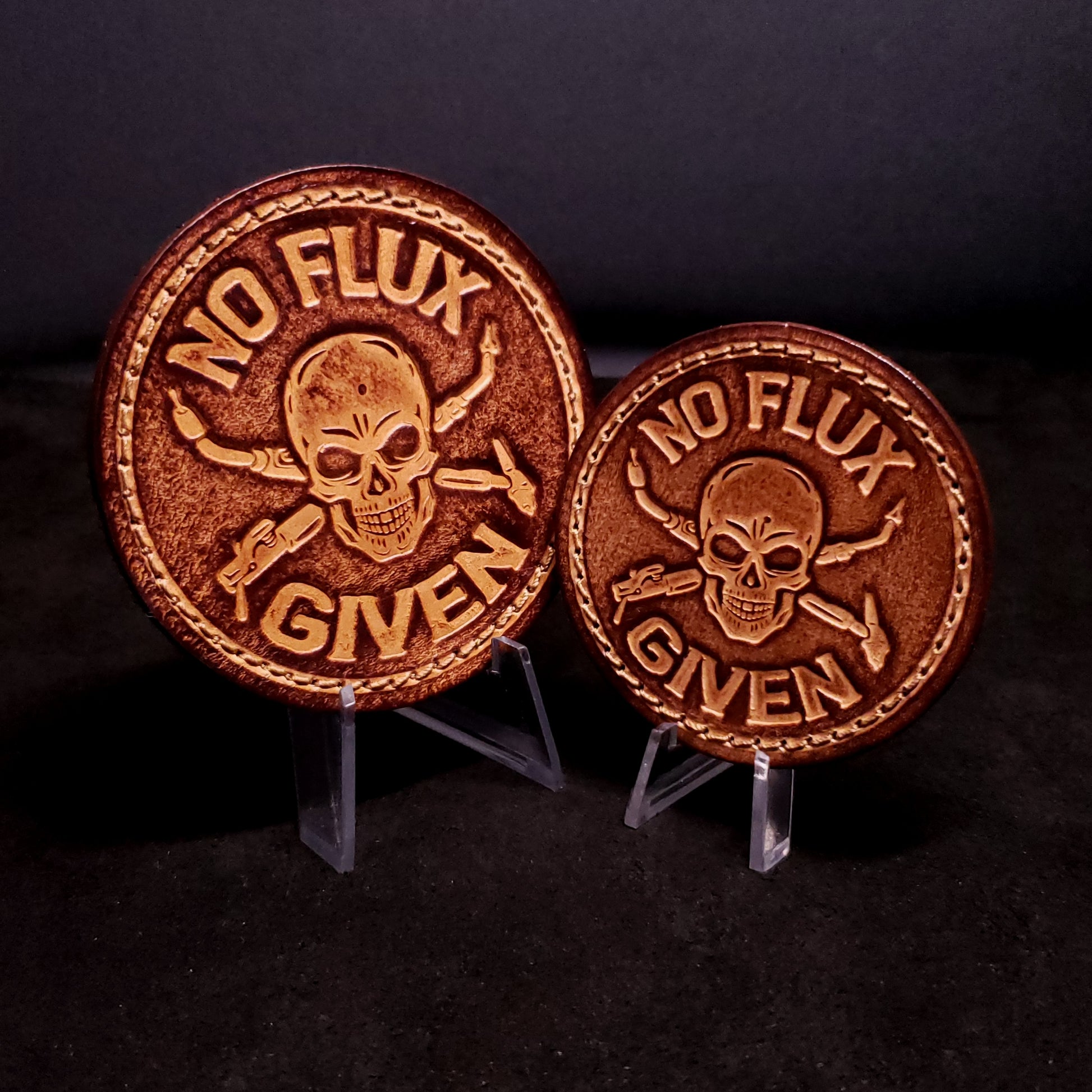 Two brown leather velcro patches embossed with text that says "No flux given", and an image of a skull with welding tools crossed behind it.
