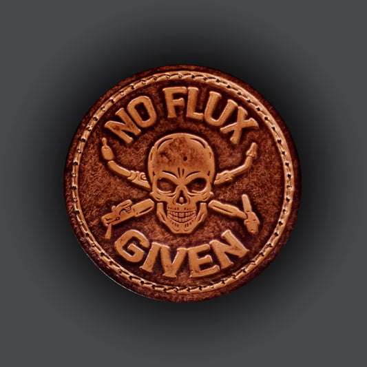 Brown leather velcro patch embossed with text that says "No flux given", and an image of a skull with welding tools crossed behind it.