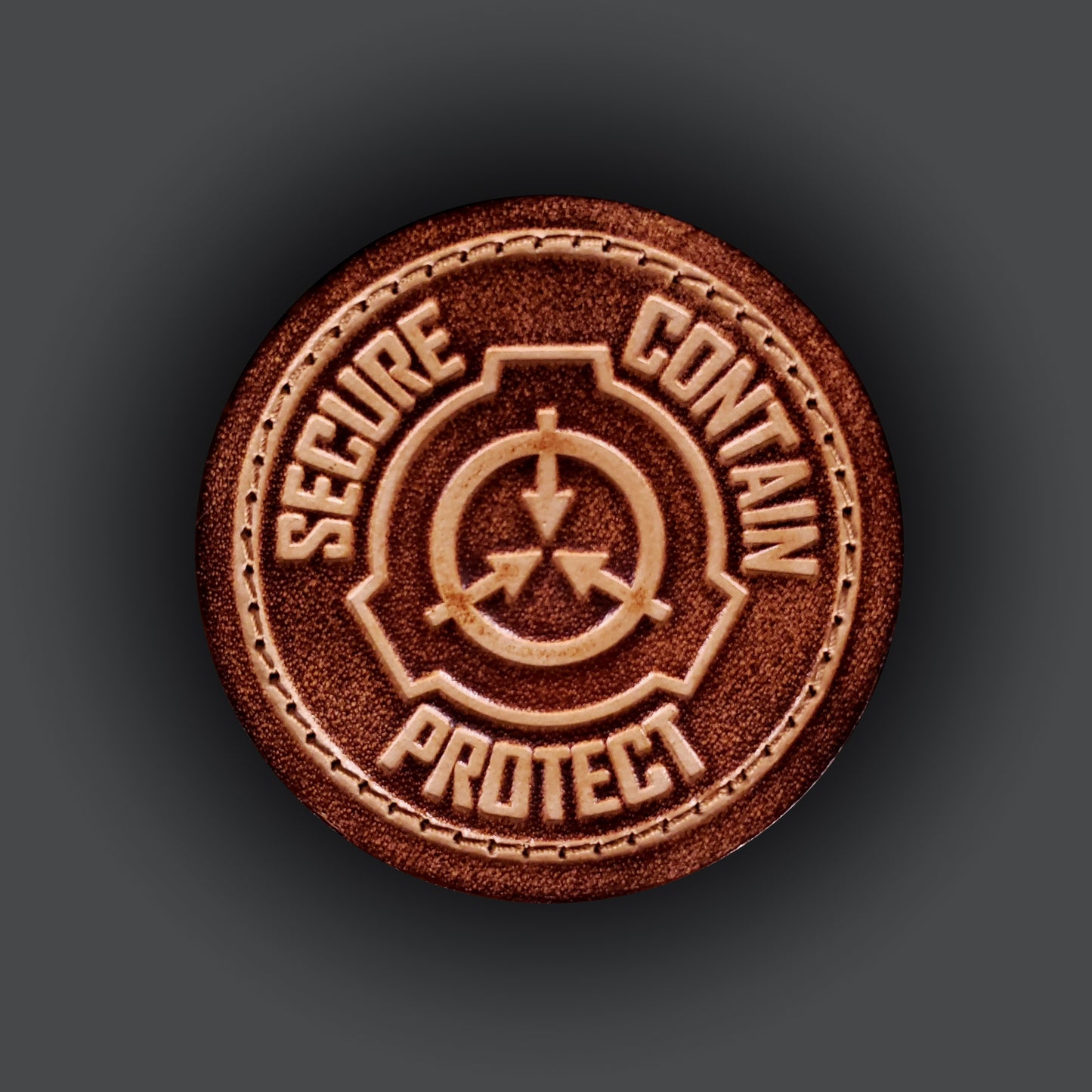 Brown leather velcro patch embossed with text that says "Secure, contain, protect", and a symbol of the fictional SCP foundation.