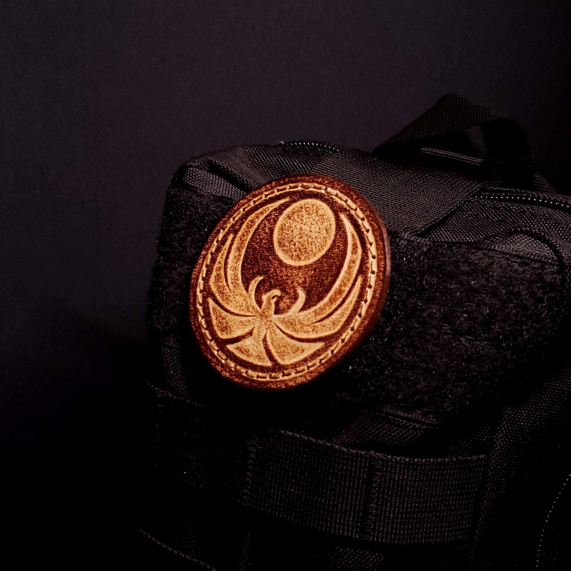 Brown leather velcro patch embossed with the Skyrim nightingale symbol from the Elder Scrolls franchise, affixed to a a bag.