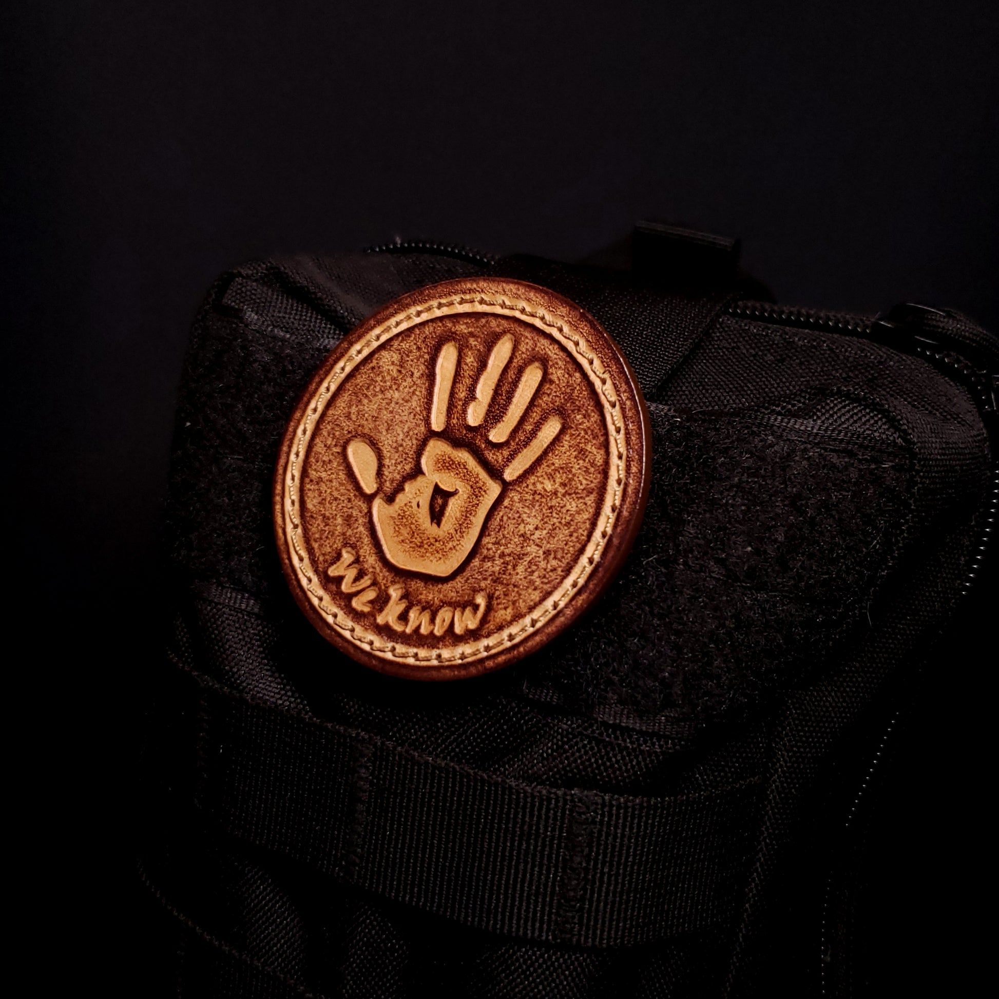 Brown leather velcro patch featuring text that says "We know", and a hand print from the Elder Scrolls franchise, affixed to a bag.