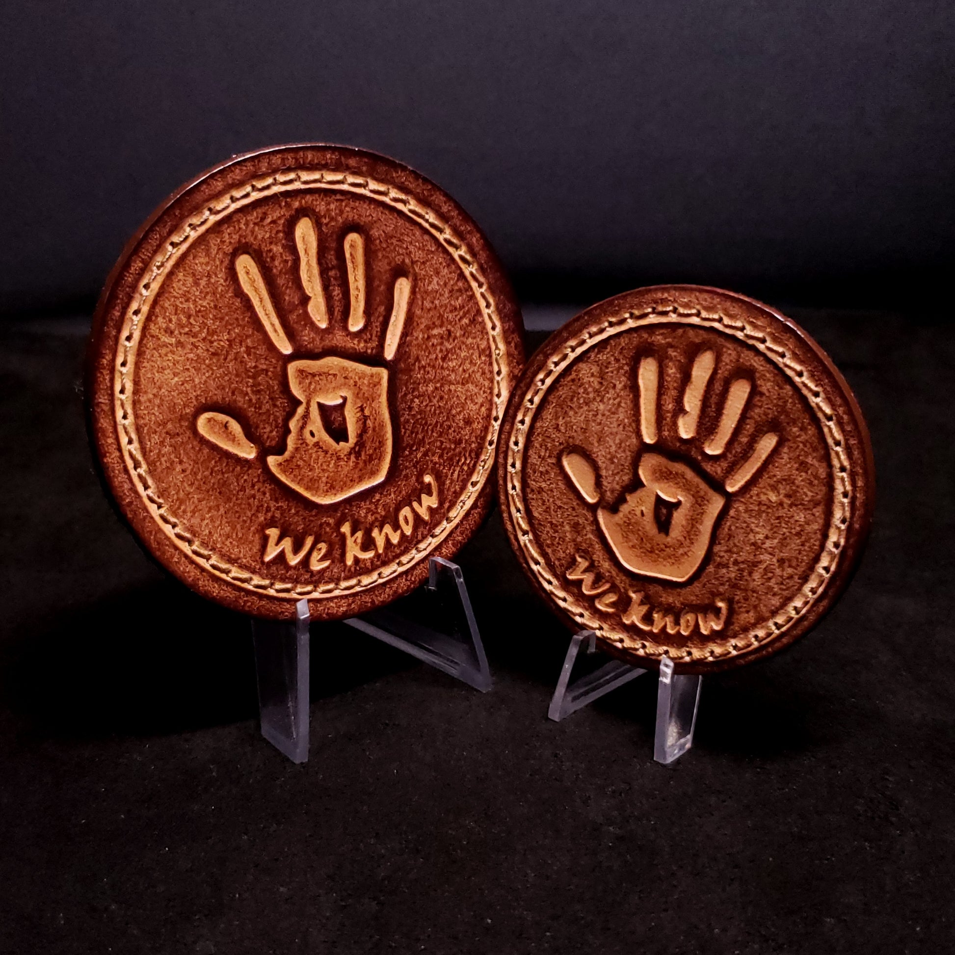Two brown leather velcro patches featuring text that says "We know", and a hand print from the Elder Scrolls franchise, posed on a black background.