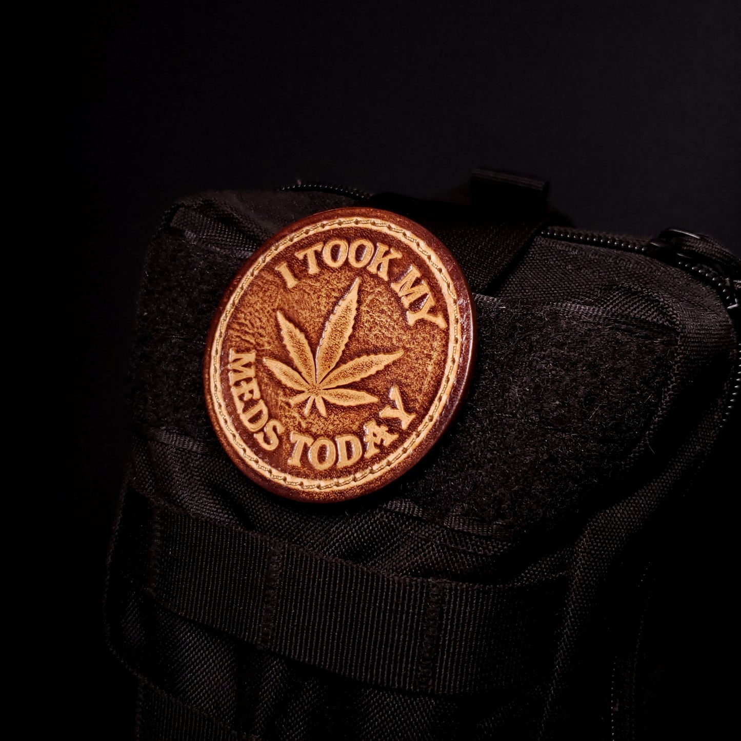 Brown leather velcro patch embossed with a five leaf plant and text that says "I took my meds today", affixed to a bag.