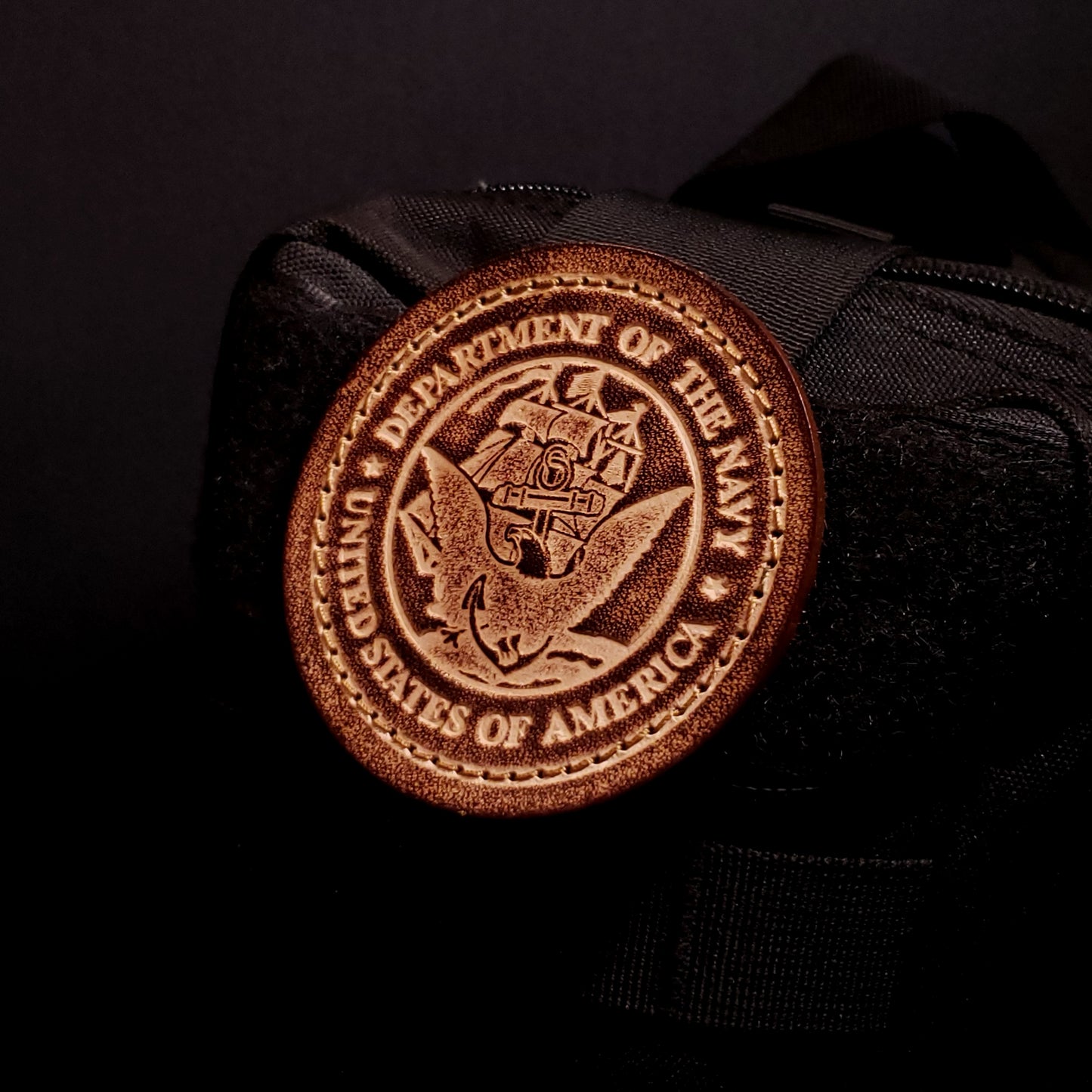Brown leather velcro patch embossed with text and the United States Navy emblem, affixed to a bag.