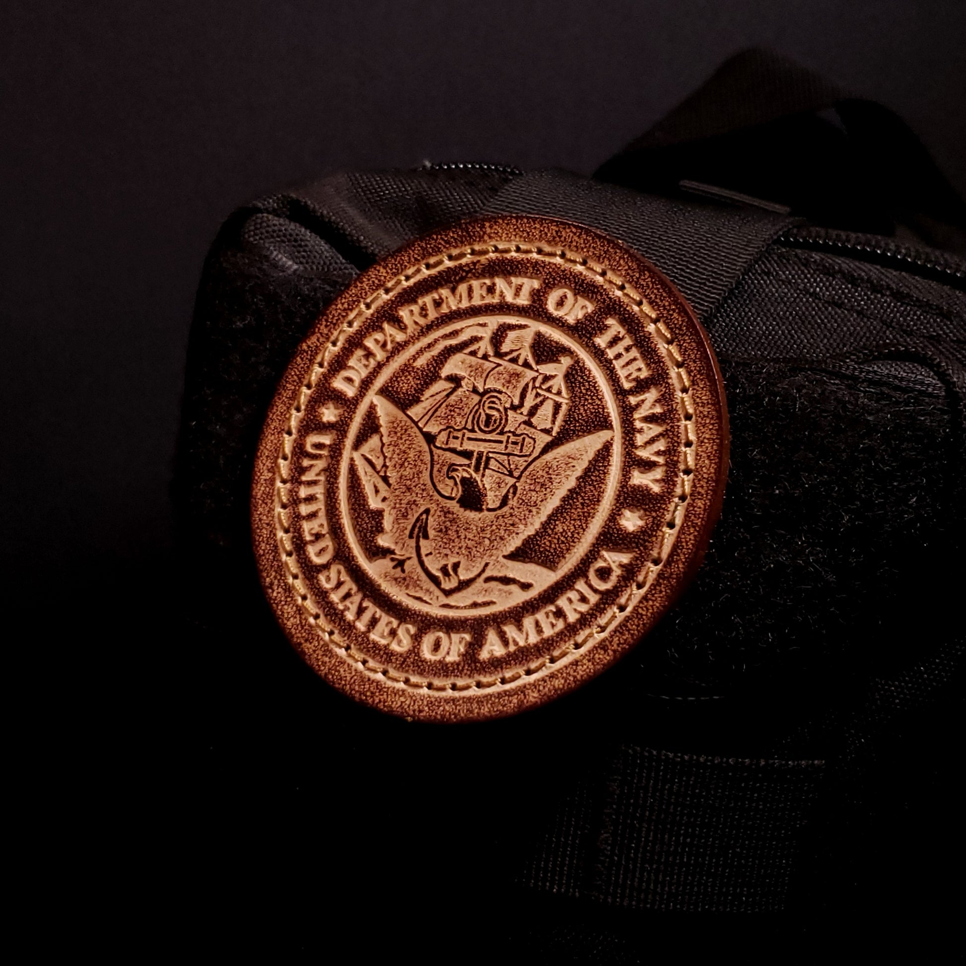Brown leather velcro patch embossed with text and the United States Navy emblem, affixed to a bag.