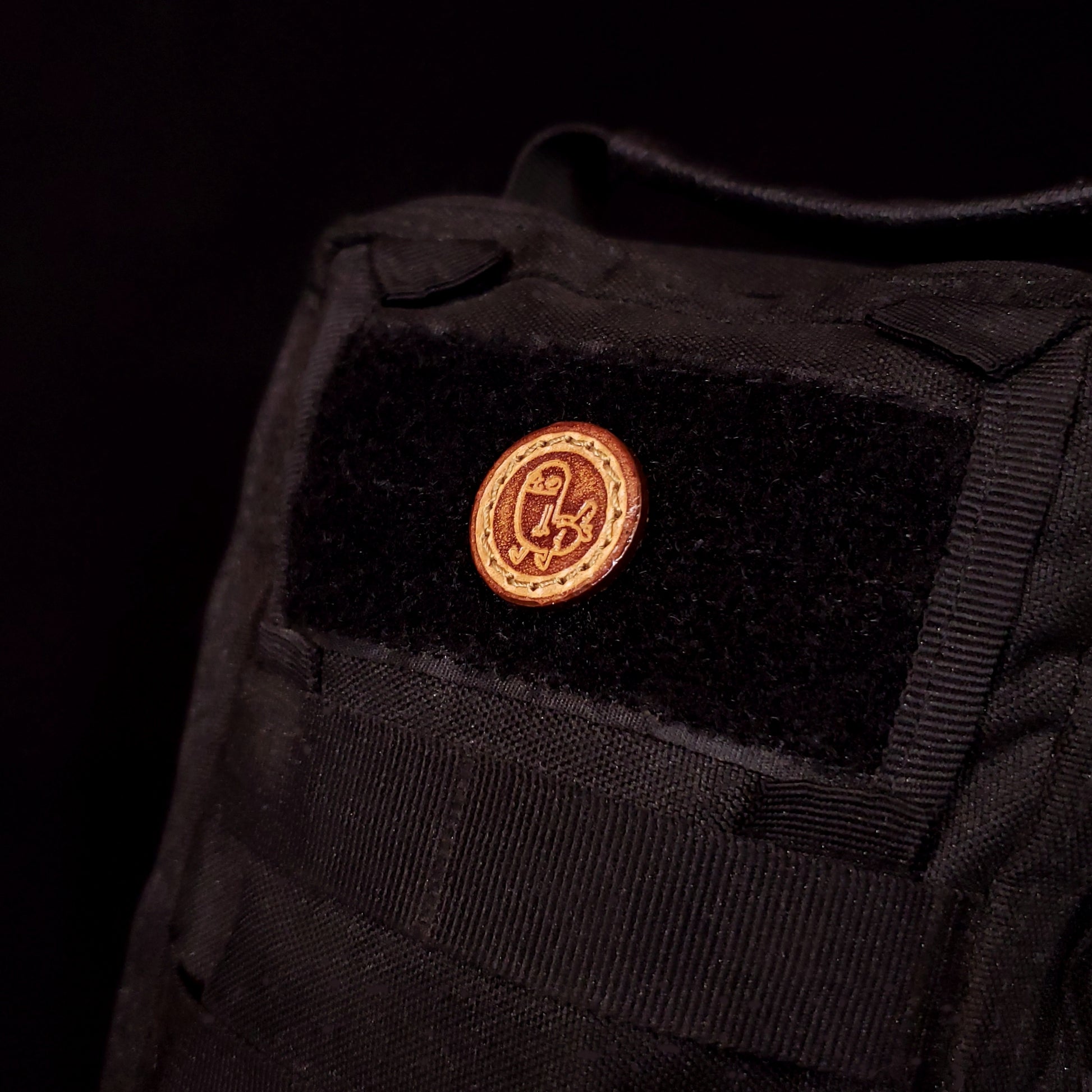 Small leather velcro patch embossed with an internet meme character called Dick Butt, affixed to a bag.