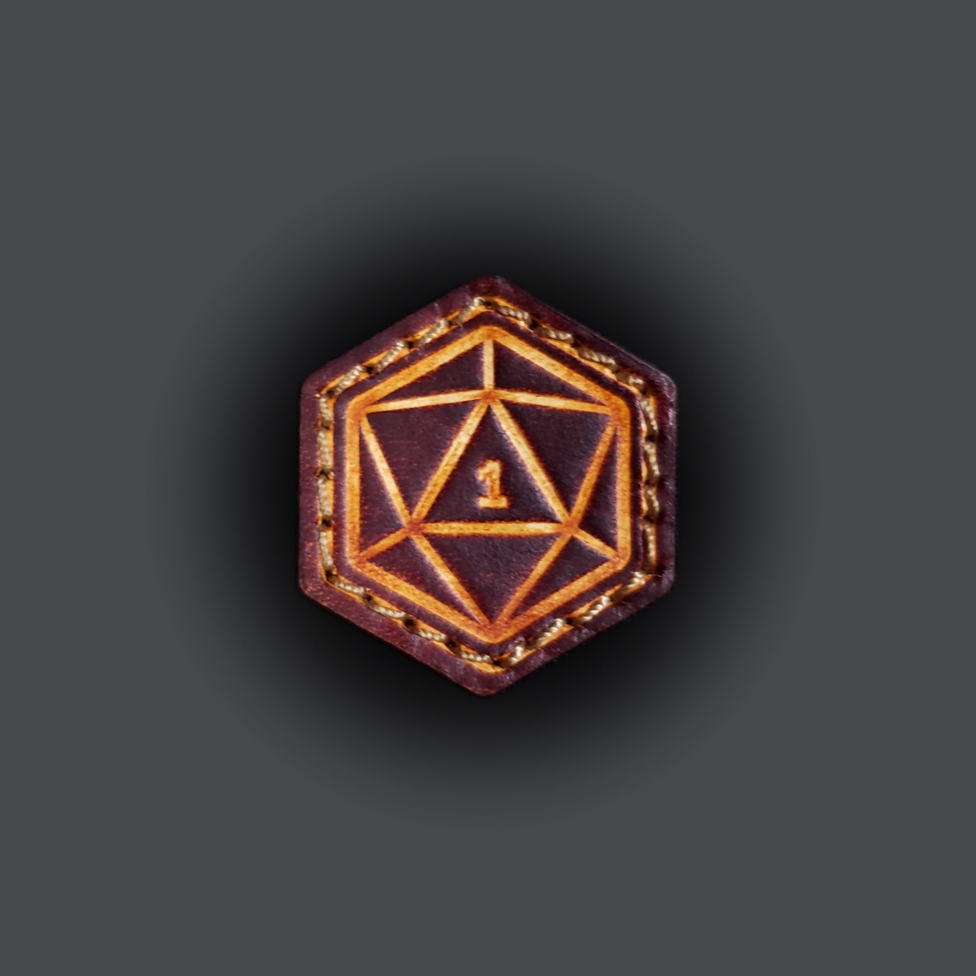 Small leather velcro patch embossed with a twenty-sided die with the number one facing up.