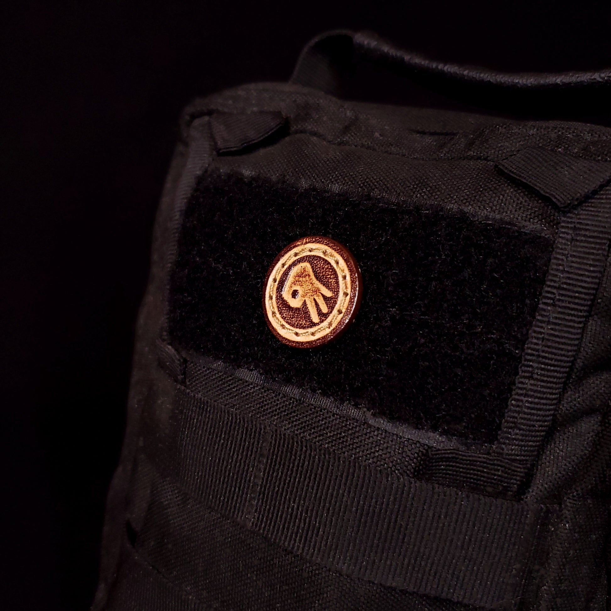 Small leather velcro patch embossed with a hand in an "okay" position up-side down, affixed to a bag.