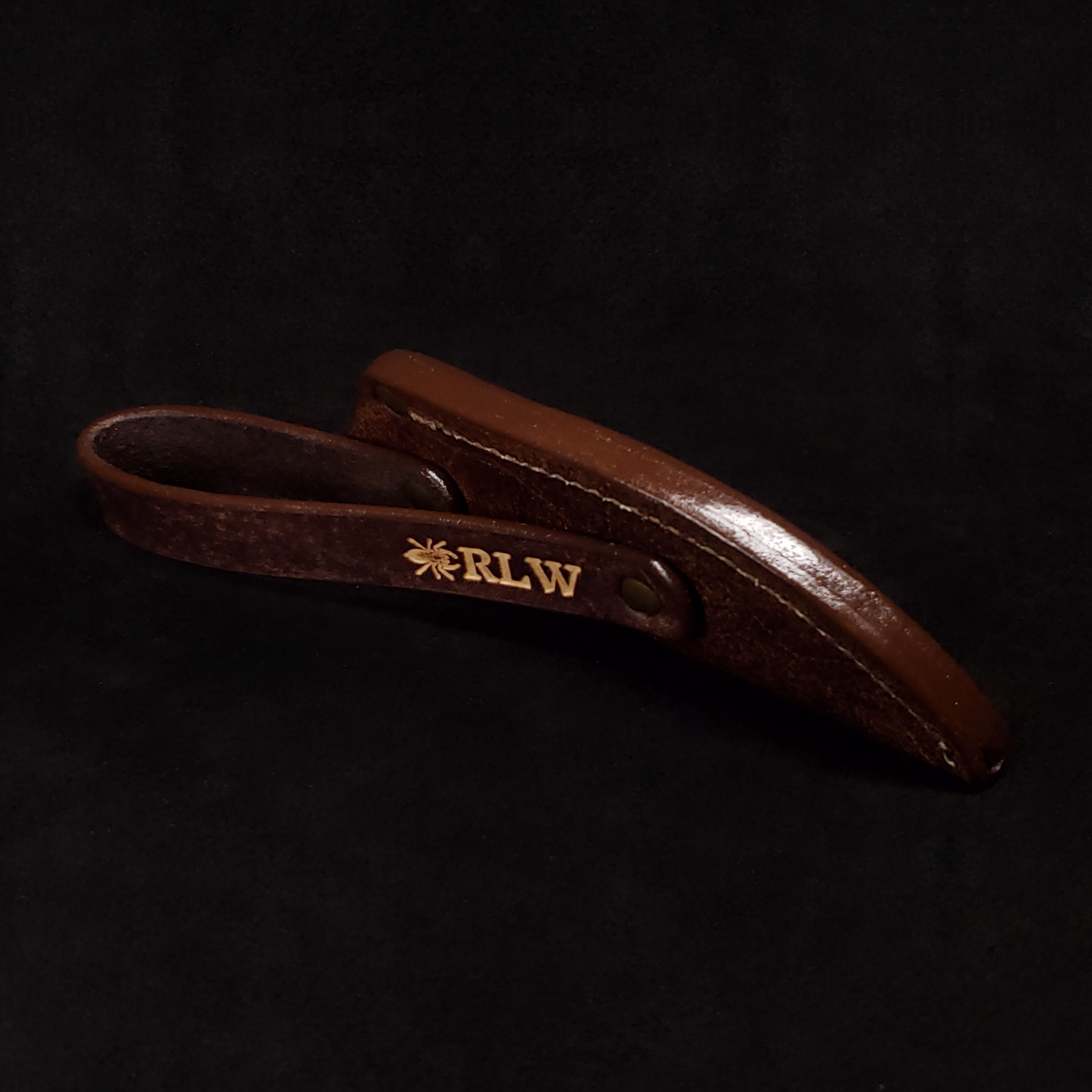 Brown leather knife sheath with a glossy edge and belt loop embossed with the Regius logo.
