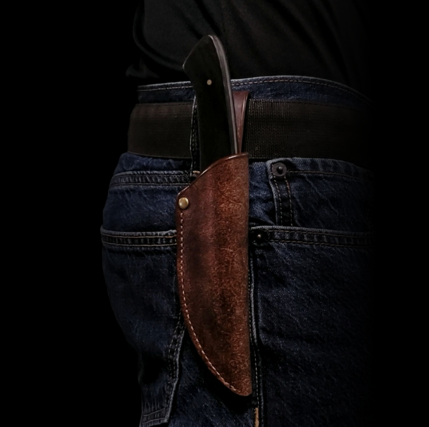Brown leather knife sheath holding a knife, affixed to the belt on a man's waist.