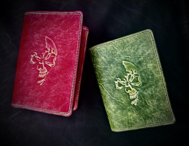 Two leather book covers, one green and one red, embossed with the skull logo of Szabo Inc.